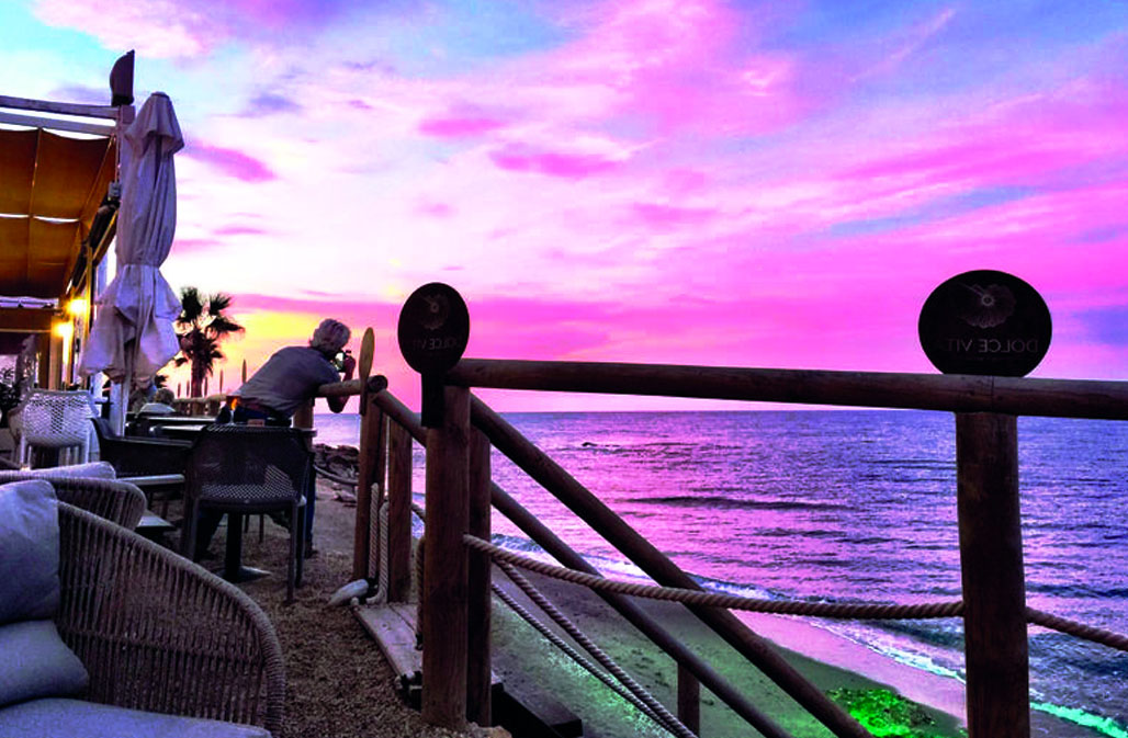 A breathtaking vista from a beachfront Mojacar restaurant overlooking the vast expanse of the Mediterranean. As the sun dips below the horizon, it casts an ethereal glow of magentas and purples across the sky, mirrored in the gentle ripples of the sea below. 
