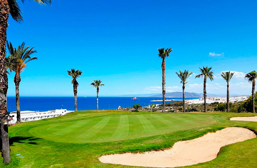 The image showcases a pristine golf course in Mojacar, with lush greens, towering palm trees, and a breathtaking view of the coastline.