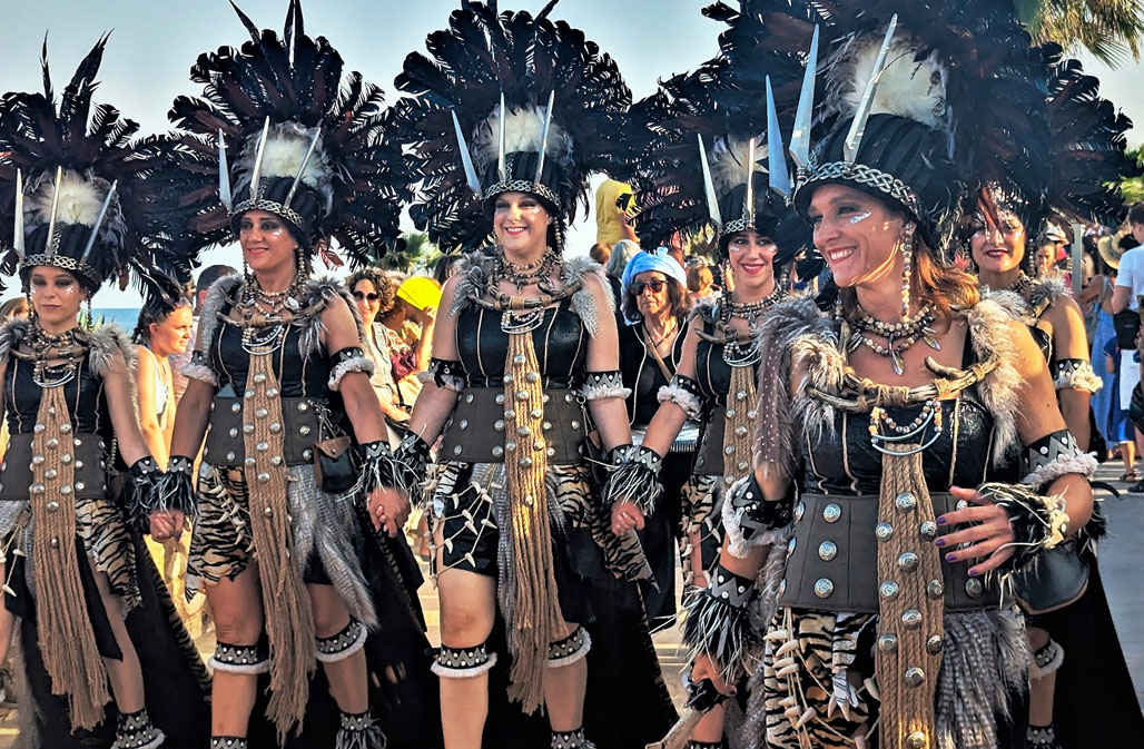 Participants dressed in elaborate tribal-inspired costumes with feathered headdresses, celebrating the Moors and Christians fiesta in Mojacar.