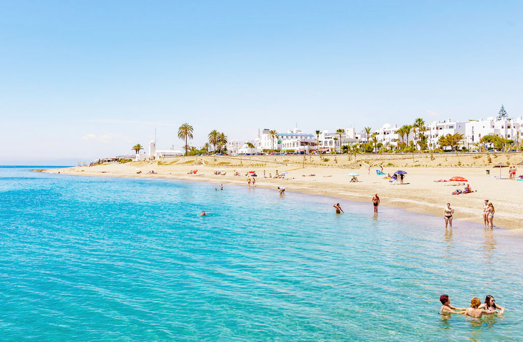 A picturesque scene from Mojácar beach, where the crystal-clear azure waters meet the golden sands, teeming with sunbathers and swimmers reveling in the serene embrace of the Mediterranean sea. 