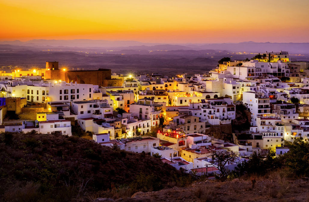 Majestic panorama of Mojacar Pueblo at twilight, where the radiant hues of the sunset backdrop a labyrinthine town filled with pristine white buildings,